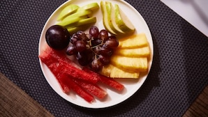 Un plato con rodajas de manzana, uvas, piña y pimiento rojo sobre un mantel tejido.
