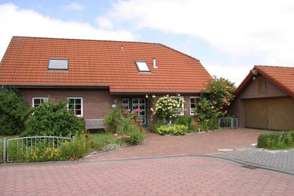 A two-story house with a red-tiled roof, a front garden with flowers, and a paved driveway.