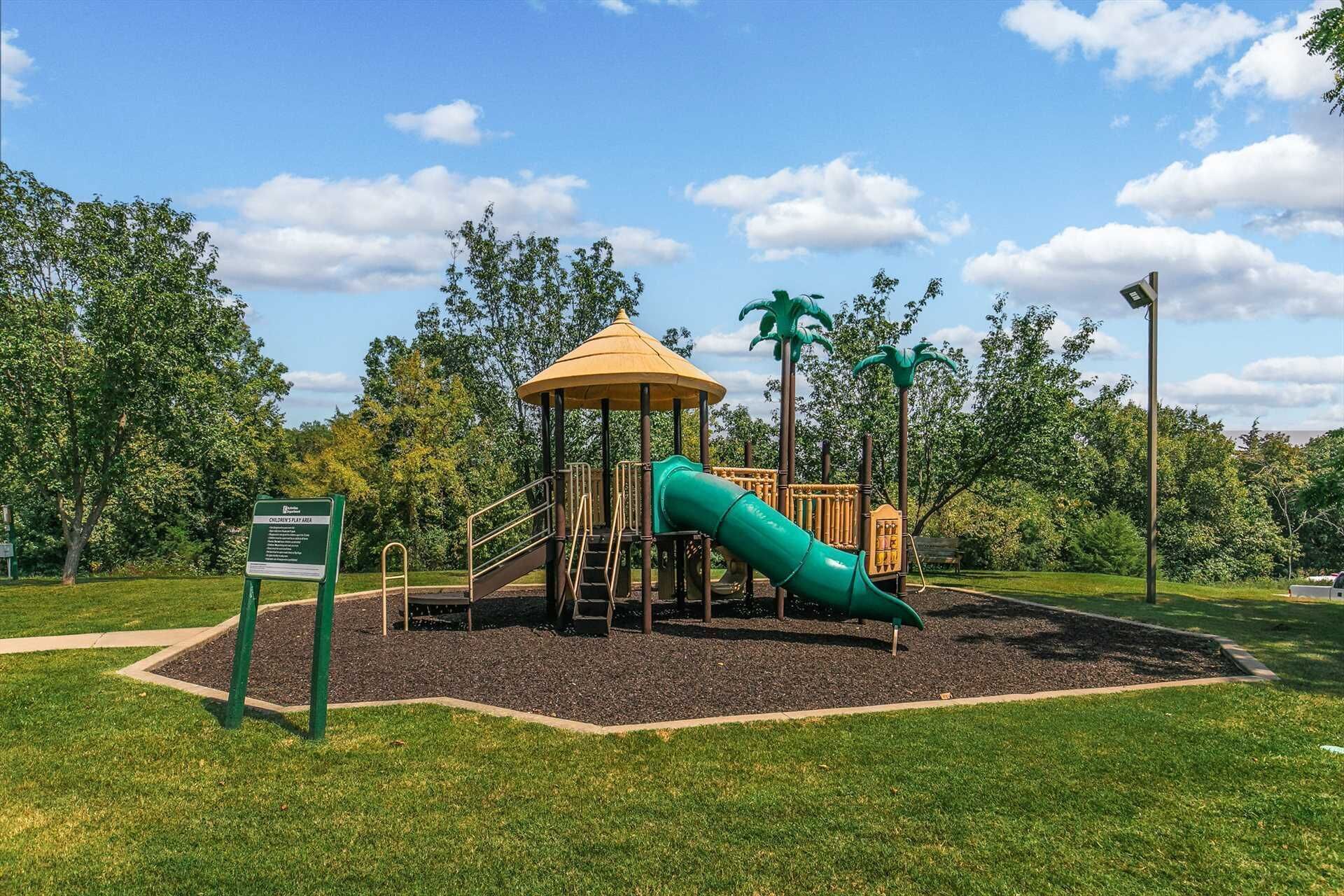 Ein Spielplatz mit Rutsche und Klettergerüst, umgeben von Gras und Bäumen.