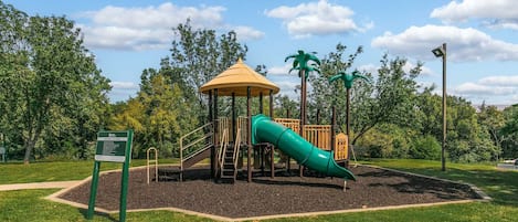 Un parque infantil con un tobogán y una estructura para escalar, rodeado de césped y árboles.