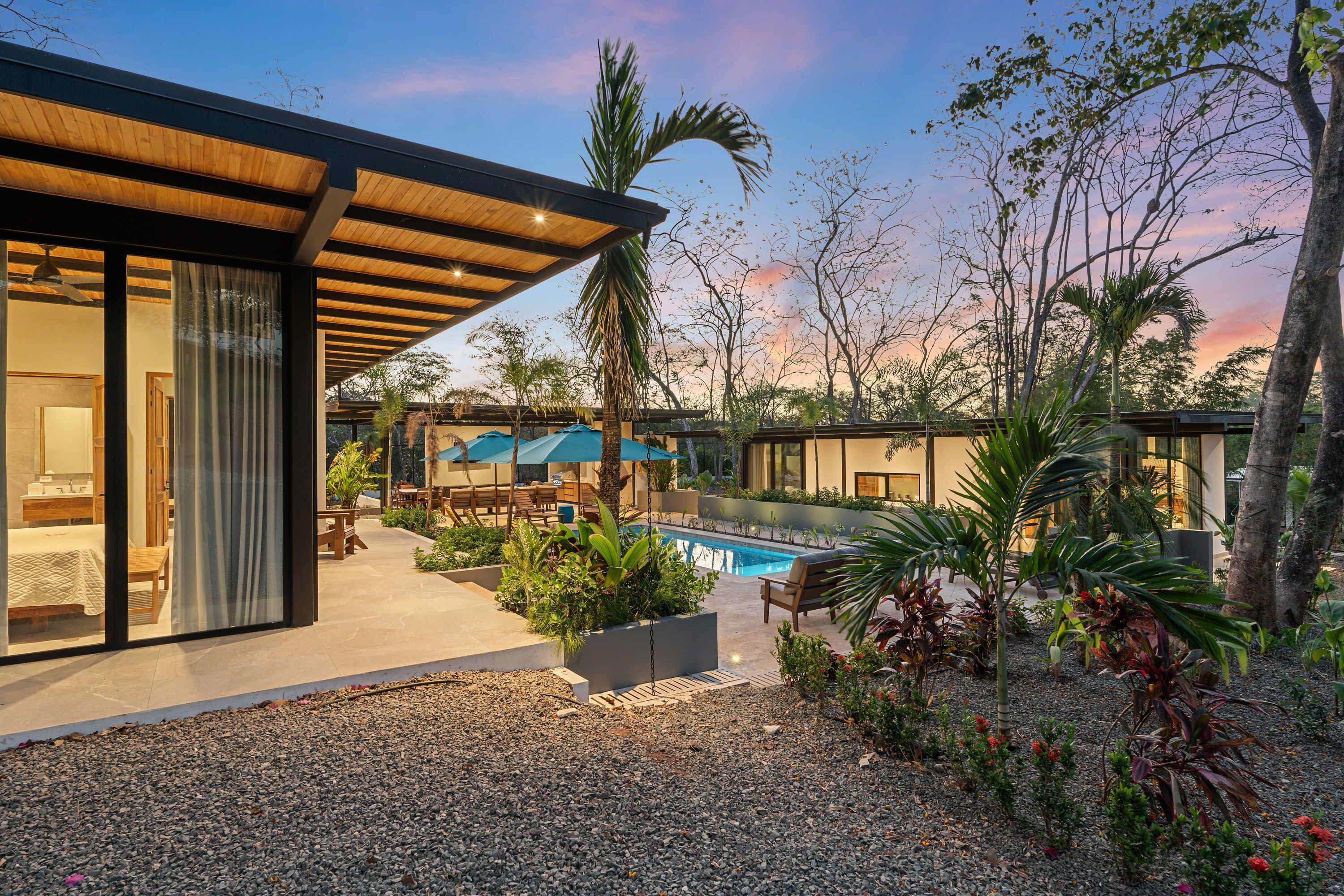 A modern building with a pool, outdoor seating, and tropical plants.