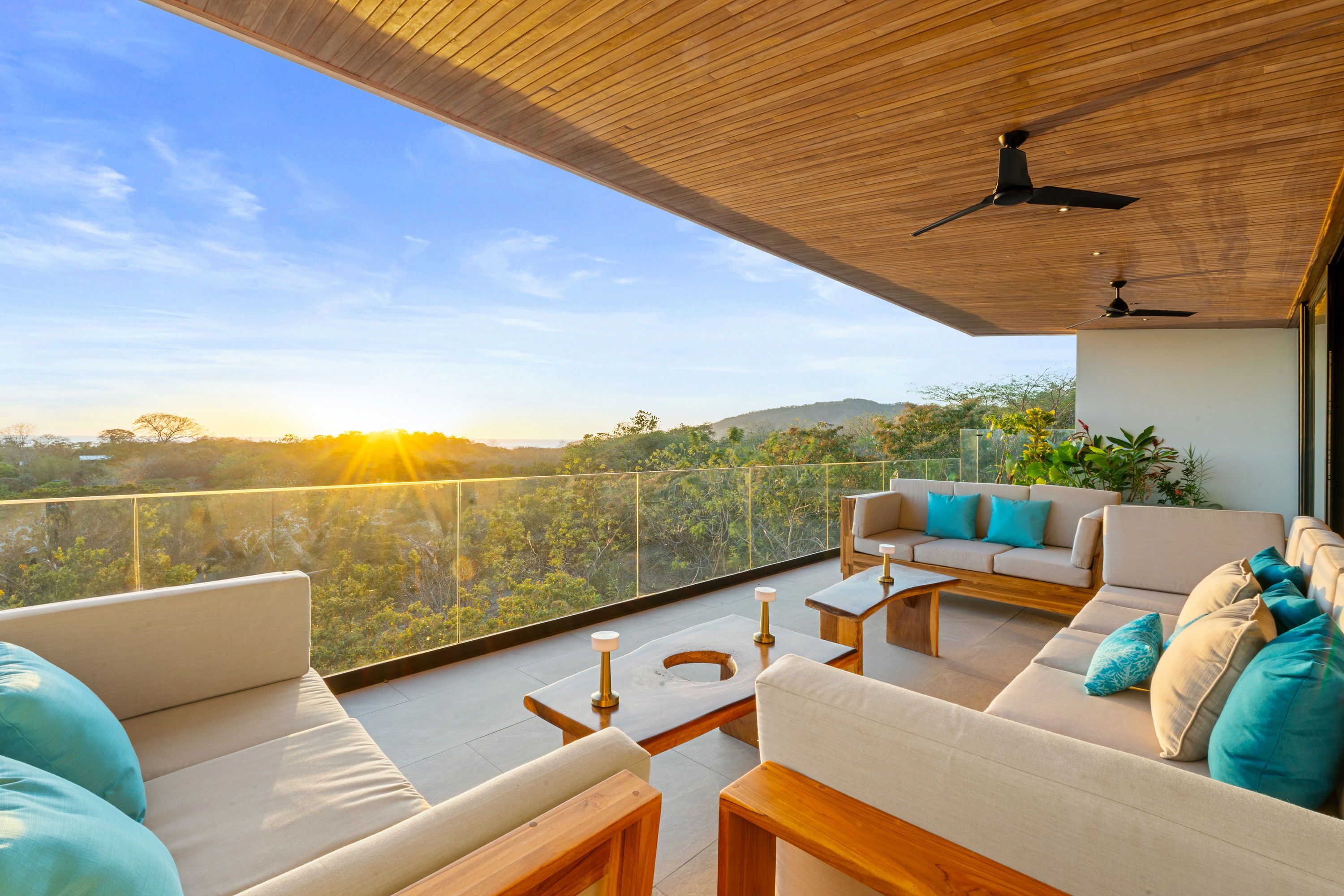 A balcony with a sofa, coffee table, and chairs, overlooking a scenic landscape with trees and hills.
