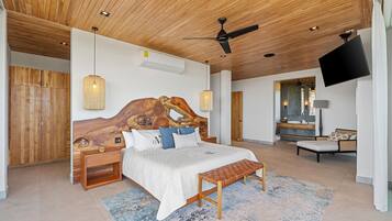 Een moderne slaapkamer met een houten hoofdbord, een groot bed, nachtkastjes, een bankje, een televisie en een badkamer met een spiegel en wastafel.