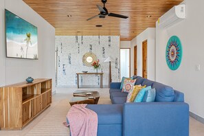 A modern living room with a blue sofa, wooden entertainment unit, and a ceiling fan.