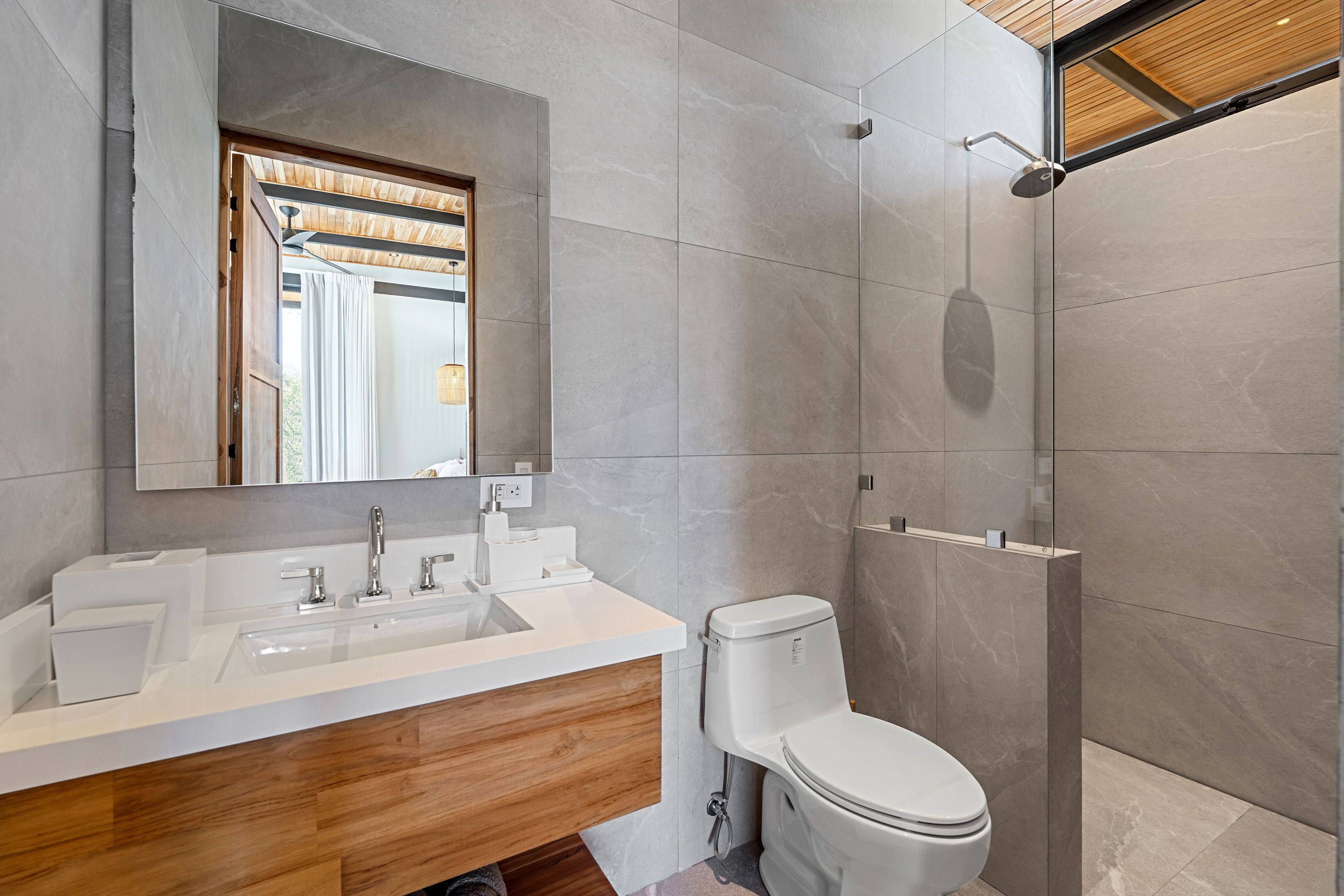 A modern bathroom with a wooden vanity, a large mirror, a toilet, and a shower area.