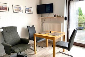 Quarto com mesa de madeira, duas cadeiras, televisão fixada na parede e quadros enquadrados na parede.