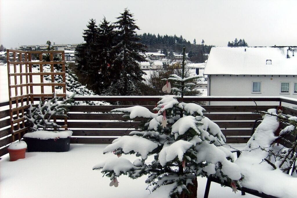 Un balcón cubierto de nieve con una valla de madera, una planta en maceta y una banca.