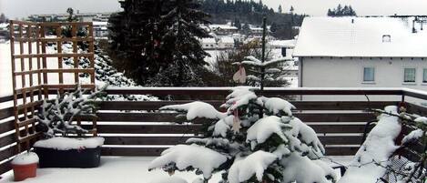 Un balcón cubierto de nieve con una valla de madera, una planta en maceta y una banca.