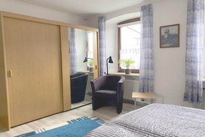 Quarto com cama, guarda-roupa, cadeira, janela com cortinas e uma pequena mesa.