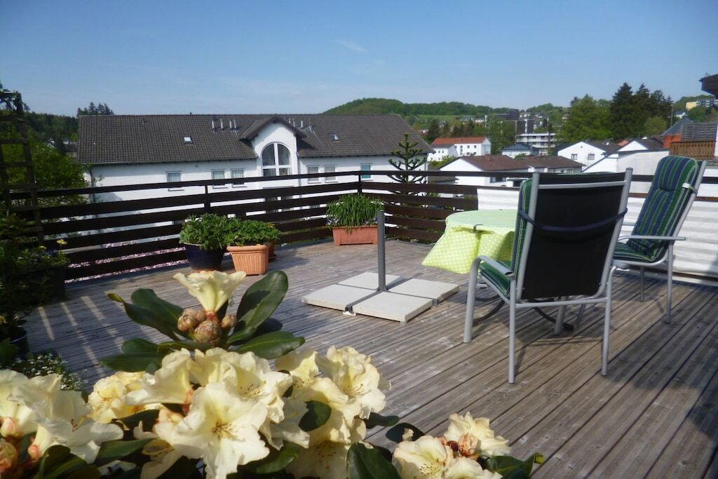 Eine Holzterrasse mit Tisch und Stühlen, umgeben von Blumentöpfen und Blumen.