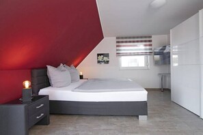 Une chambre à coucher moderne avec un lit, une table de chevet et un mur d’accent rouge.