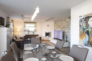 A modern living room with a dining area, a fireplace, and a television. - Villa Paradiso on the lake (Göhren - Lebbin)