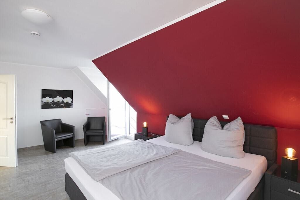 Een moderne slaapkamer met een groot bed, een rode accentmuur en een nachtkastje met een lamp.