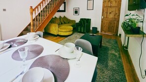 Un comedor con una mesa preparada para cuatro, una escalera, un sofá verde y una puerta de madera.