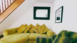 Una habitación con un sofá verde, un sillón a rayas y una escalera de madera.