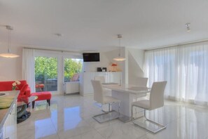 A modern kitchen with a dining area, a TV mounted on the wall, and a large window with curtains. - Holiday apartment in Sylt with 1 bedroom (Wenningstedt)