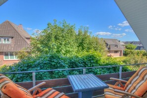 Ein Balkon mit Tisch und Stühlen, umgeben von Grünpflanzen und Häusern im Hintergrund.