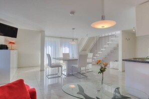 Ein modernes Wohnzimmer mit einem Glastisch, einem roten Sofa und einem Essbereich mit weißen Stühlen.