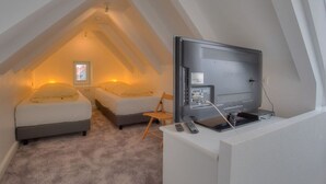 Quarto com televisão, duas camas, uma cadeira e janela.