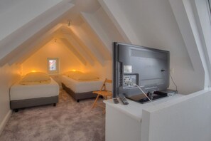 Ein Schlafzimmer mit Fernseher, zwei Betten, einem Sessel und einem Fenster.