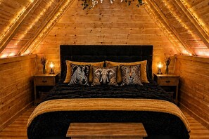 Une chambre avec un plafond en pente, des murs en bois, un lit agrémenté d’oreillers à motifs et des lampes de chevet.