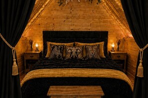 Un dormitorio acogedor con techo de madera, una cama grande con almohadas estampadas y lámparas de noche.