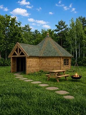 Una cabaña rústica de madera con techo verde, una puerta de madera y una mesa de picnic con una fogata.