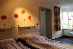 A hotel room with two beds, a window with curtains, and wall-mounted flower decorations. - Schönberger-Strand -Boldt (Schönbergerstrand)
