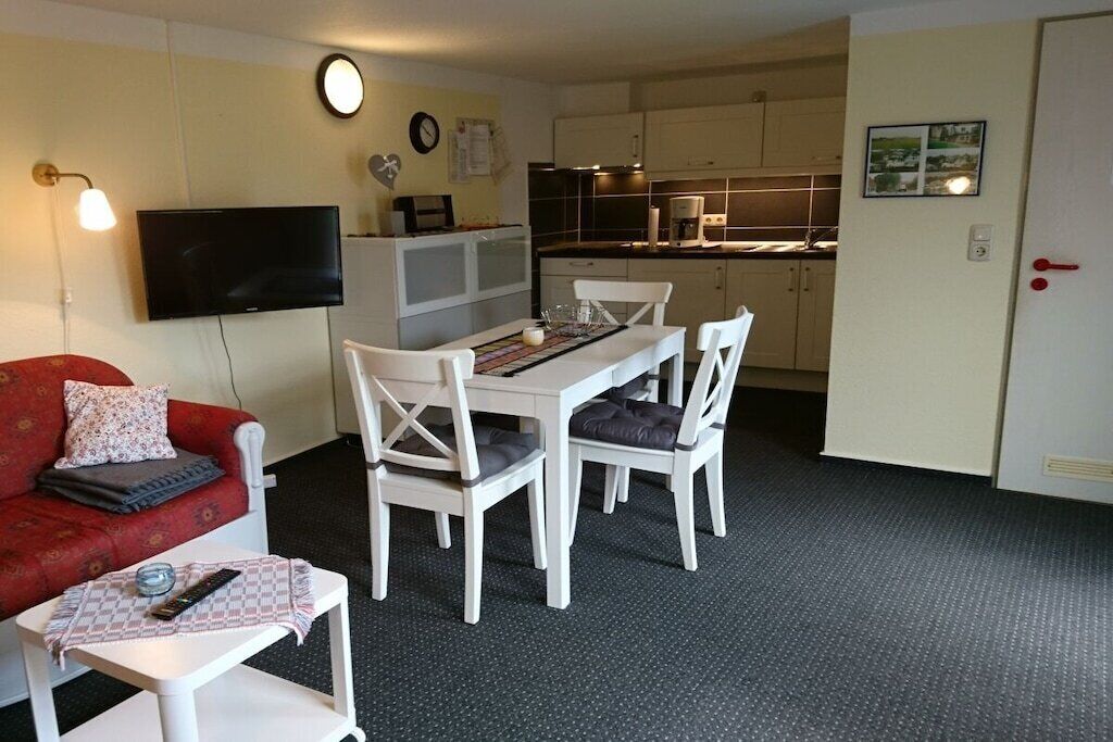 Un espace de vie compact comprenant un coin repas, une kitchenette et un téléviseur fixé au mur.