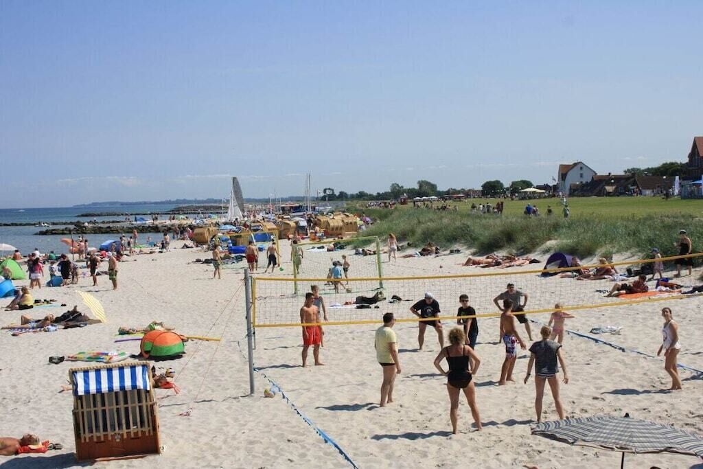 Een strand met een volleybalnet, mensen op het strand en een zeilboot op de achtergrond.