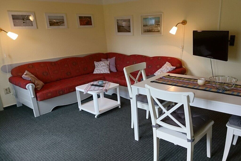 A living room with a red sofa, white chairs, a small table, and a television.