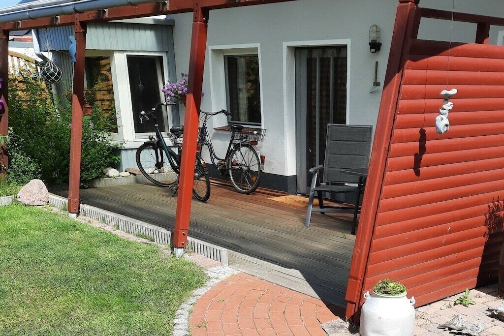 Une terrasse en bois avec deux vélos, une chaise et un petit pot blanc.