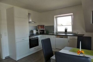 A modern kitchen with white cabinets, a microwave, an oven, and a window providing natural light. - Holiday apartment with 2 bedrooms (Rieste)