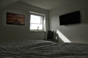 Ein Schlafzimmer mit einem Bett, einem Fenster, einem an der Wand befestigten Fernseher und einem Gemälde.