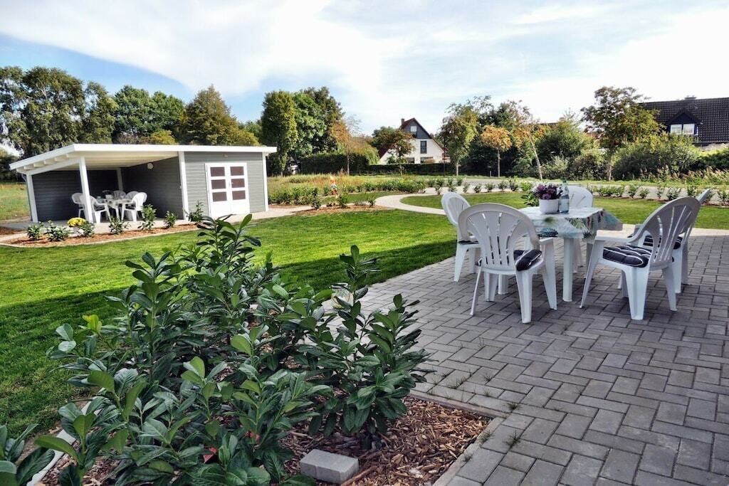 Uma área de pátio com mesa e cadeiras, cercada por um gramado bem cuidado e um pequeno galpão.