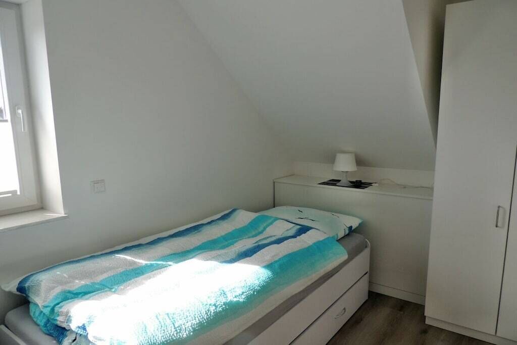 Una habitación pequeña con cama individual, ventana, mesita de noche con lámpara y armario.