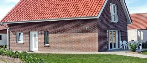 A brick building with a red-tiled roof, a white door, and a small patio with outdoor furniture.