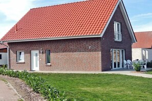 Un bâtiment en briques surmonté d’un toit de tuiles rouges, avec une porte blanche et un petit patio aménagé avec du mobilier d’extérieur.