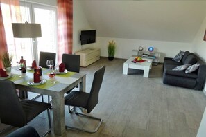 A modern living room with a dining area, a flat-screen TV mounted on the wall, a sofa, and a coffee table. - Holiday apartment with 2 bedrooms (Rieste)