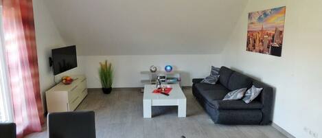 A modern living room with a grey sofa, a white coffee table, a flat-screen TV, and a painting on the wall.