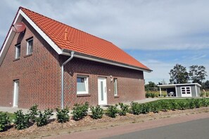 A single-story brick building with a red-tiled roof, a small porch, and a well-maintained garden. - Holiday apartment with 2 bedrooms (Rieste)