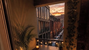 Ein Balkon mit Blick auf einen Sonnenuntergang, einem Blumentopf, einem Tisch mit Stuhl und einem kleinen Bücherregal.