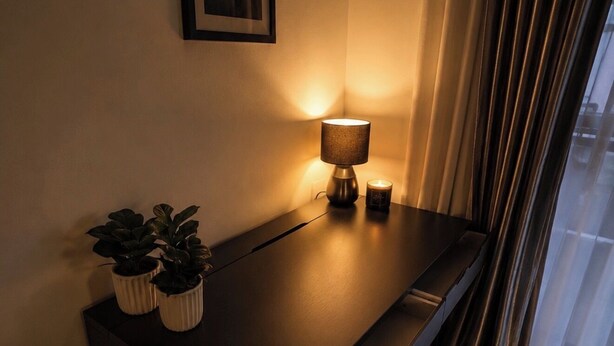 Un bureau en bois foncé, sur lequel se trouvent une lampe, deux plantes en pot et un tableau encadré accroché au mur.