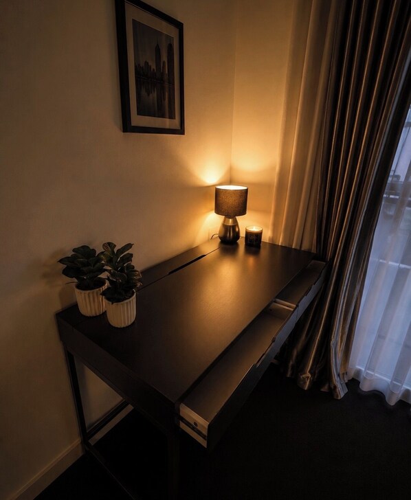 A dark wooden desk with a lamp, two potted plants, and a framed picture on the wall. - The One Space (Carlton)