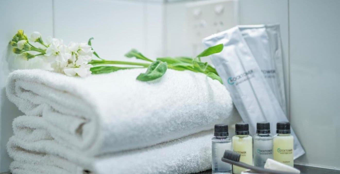 A stack of white towels, a bunch of white flowers, and a few bottles of lotion on a tray.
