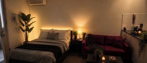 Ein Schlafzimmer mit einem Bett, einem Nachttisch, einer Lampe und einem roten Sofa.