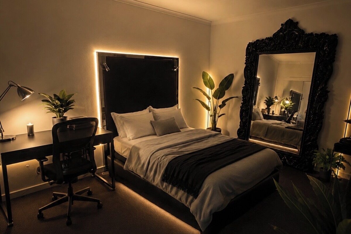 A bedroom with a bed, desk, chair, and a large mirror.