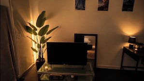 Ein Wohnzimmer mit einem Flachbildfernseher auf einem Glastisch, einer Topfpflanze und drei gerahmten Bildern an der Wand.