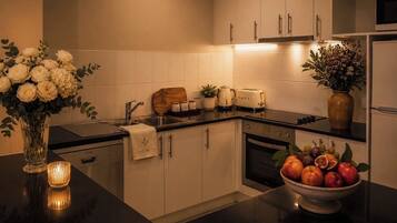 A modern kitchen with white cabinets, a black countertop, a toaster, a sink, and a bowl of fruit.