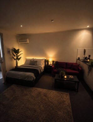 A bedroom with a bed, bedside table, lamp, and a red sofa. - The One Space (Carlton)